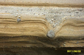 Fig. 1: Strati rocciosi alternati: in grigio un deposito piroclastico ricco in potassio e sodio; in ocra un deposito di “Surge” con la presenza di un’Impattite